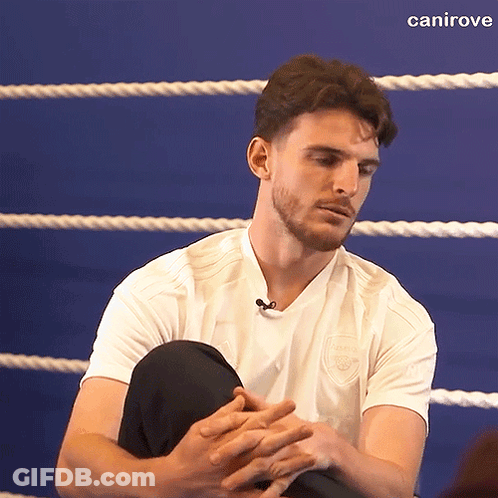 A Man In A White Shirt Is Sitting In A Boxing Ring With His Hands Folded In Front Of Him GIF