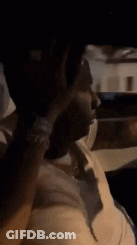 A Man In A White Shirt Is Sitting In A Car Smoking A Cigarette . GIF
