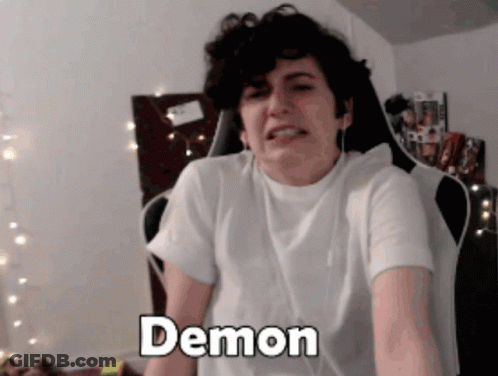 A Man In A White Shirt Is Sitting In A Chair And The Word Demon Is On His Chest GIF