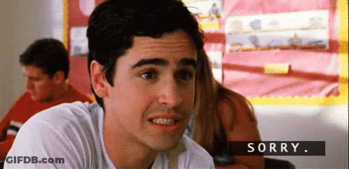 A Man In A White Shirt Is Sitting In A Classroom And Making A Face . GIF