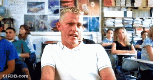 A Man In A White Shirt Is Sitting In A Classroom With A Group Of Students . GIF