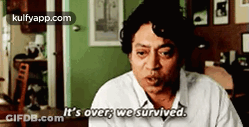 A Man In A White Shirt Is Sitting In A Living Room And Saying `` It 'S Over We Survived '' . GIF