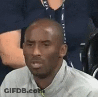 A Man In A White Shirt Is Sitting In A Stadium With A Group Of People . GIF