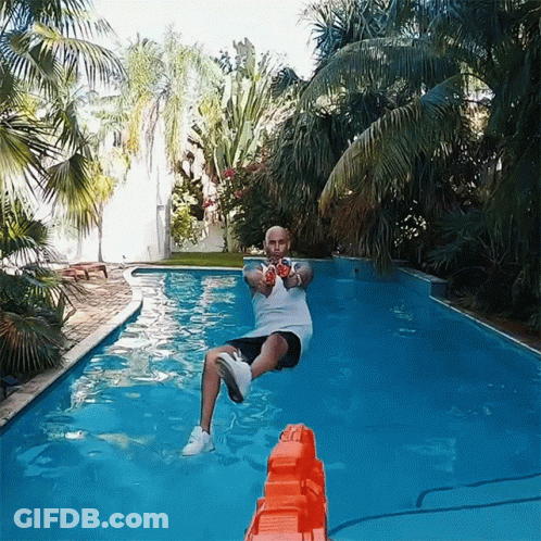 A Man In A White Shirt Is Sitting In A Swimming Pool Holding A Nerf Gun GIF