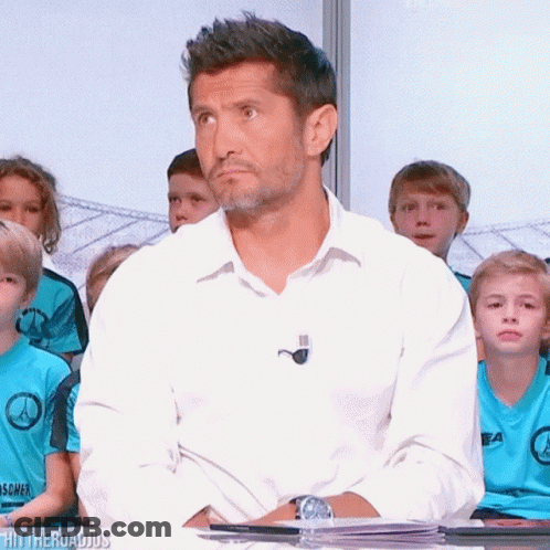 A Man In A White Shirt Is Sitting In Front Of A Group Of Children Wearing Blue Shirts That Say ' Ea ' GIF
