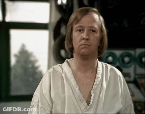 A Man In A White Shirt Is Sitting In Front Of A Laundry Machine GIF