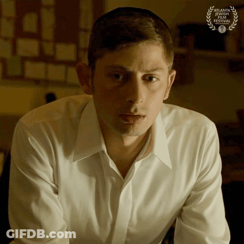Man In White Shirt Sitting In Front Of Laurel Wreath GIF