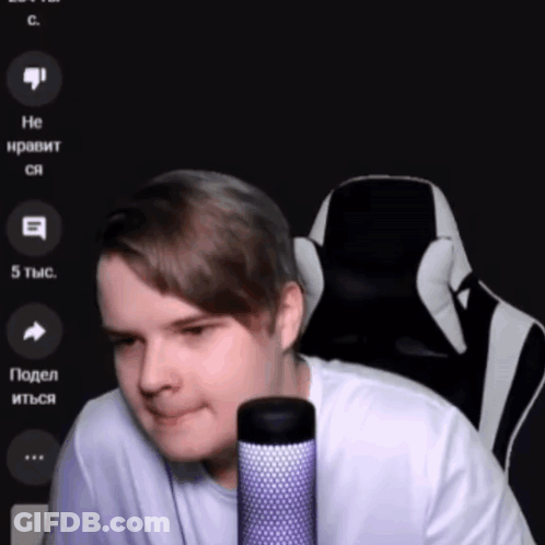 A Man In A White Shirt Is Sitting In Front Of A Microphone With A Black And White Chair Behind Him GIF