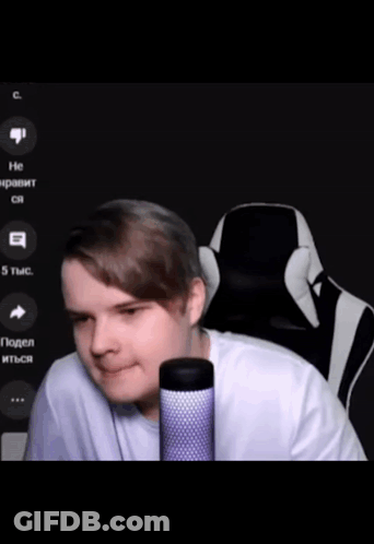 A Man In A White Shirt Is Sitting In Front Of A Microphone With A Black And White Chair Behind Him GIF