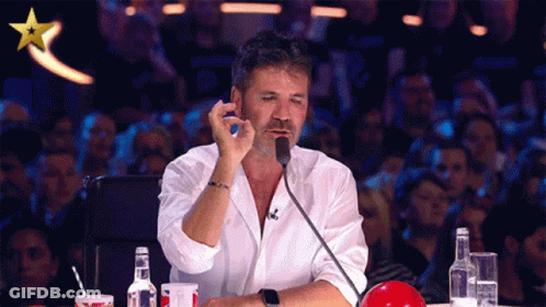 A Man In A White Shirt Is Sitting In Front Of A Microphone With A Gold Star Above Him GIF