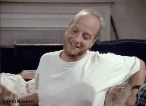 A Man In A White Shirt Is Sitting On A Couch Smiling GIF