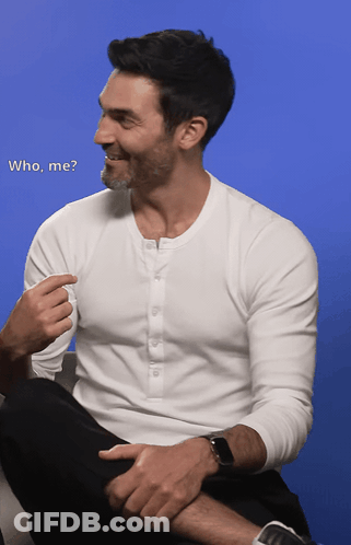 A Man In A White Shirt Is Sitting On A Couch Talking To Another Man With The Words " Who Me " Written Below Him GIF
