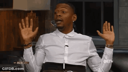 A Man In A White Shirt Is Sitting On A Couch With His Hands In The Air GIF