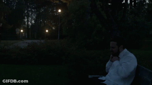 A Man In A White Shirt Is Sitting On A Park Bench GIF