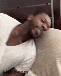 A Man In A White Shirt Is Sleeping On A Bed With His Head On A Pillow GIF