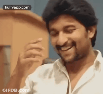 A Man In A White Shirt Is Smiling And Laughing While Standing In Front Of A Microphone . GIF