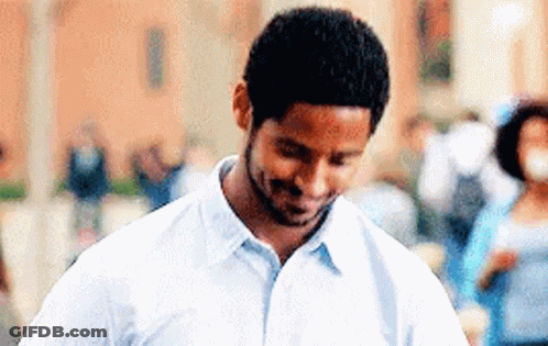 A Man In A White Shirt Is Smiling And Looking Down At Something . GIF