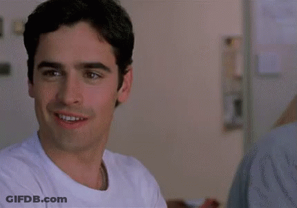 A Man In A White Shirt Is Smiling In A Room . GIF