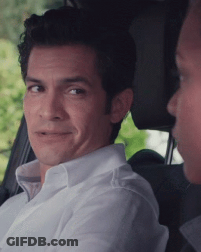 A Man In A White Shirt Is Smiling While Sitting In The Back Seat Of A Car GIF