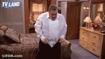A Man In A White Shirt Is Standing In A Bedroom With A Dresser And A Bed . GIF