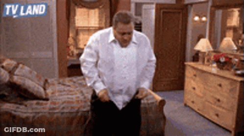 A Man In A White Shirt Is Standing In A Bedroom With A Tv Land Logo On The Wall GIF