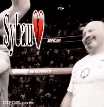 A Man In A White Shirt Is Standing In A Boxing Ring With A Crowd In The Background . GIF