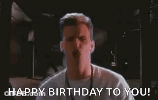 A Man In A White Shirt Is Standing In A Dark Room And Says `` Happy Birthday To You ! '' GIF