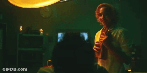 A Man In A White Shirt Is Standing In A Dark Room Holding A Glass Of Wine . GIF