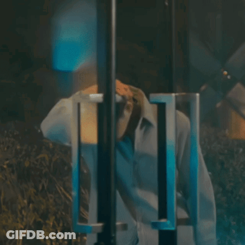 A Man In A White Shirt Is Standing In A Dark Room With His Head Down GIF
