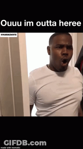 A Man In A White Shirt Is Standing In A Doorway . GIF