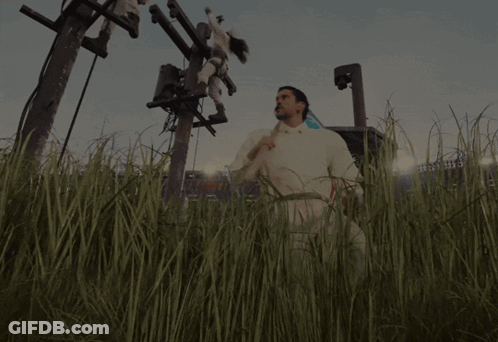 A Man In A White Shirt Is Standing In A Field With A Stadium In The Background GIF
