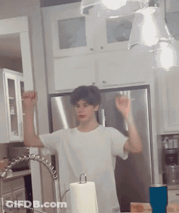A Man In A White Shirt Is Standing In A Kitchen Near A Paper Towel Dispenser GIF