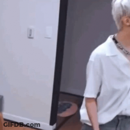 A Man In A White Shirt Is Standing In A Room Next To A Doorway . GIF