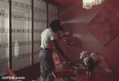 A Man In A White Shirt Is Standing In A Room With A Red Light On The Ceiling GIF