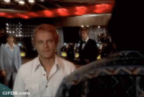 A Man In A White Shirt Is Standing In A Room With Other Men GIF