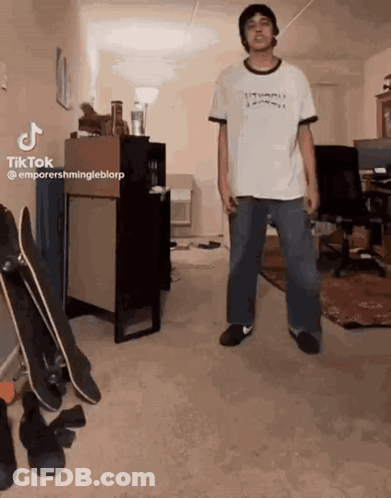 A Man In A White Shirt Is Standing In A Room With Skateboards . GIF