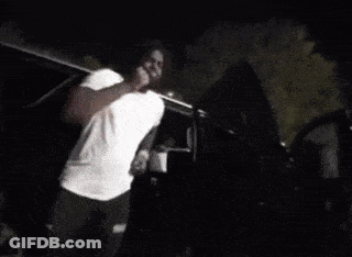 A Man In A White Shirt Is Standing In Front Of A Black Suv At Night . GIF