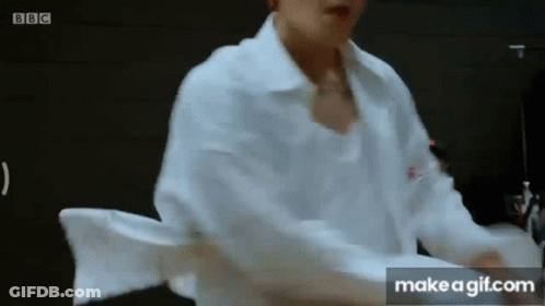 A Man In A White Shirt Is Standing In Front Of A Black Wall . GIF