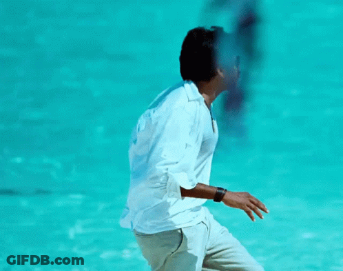 A Man In A White Shirt Is Standing In Front Of A Blue Water GIF