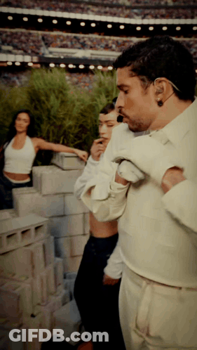 A Man In A White Shirt Is Standing In Front Of A Brick Wall GIF