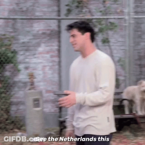 A Man In A White Shirt Is Standing In Front Of A Brick Wall And Talking To Someone . GIF