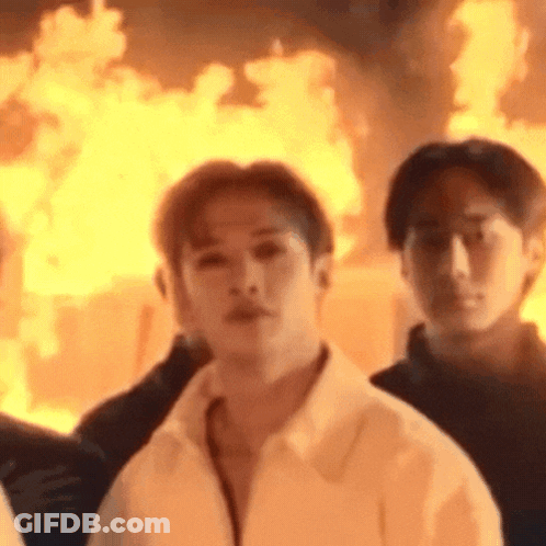 A Man In A White Shirt Is Standing In Front Of A Burning Building . GIF