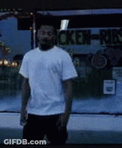 A Man In A White Shirt Is Standing In Front Of A Chicken-Munch Sign GIF