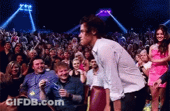 A Man In A White Shirt Is Standing In Front Of A Crowd Of People At A Concert . GIF