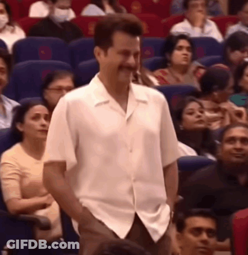 A Man In A White Shirt Is Standing In Front Of A Crowd Of People In An Auditorium . GIF