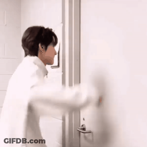 A Man In A White Shirt Is Standing In Front Of A Door . GIF