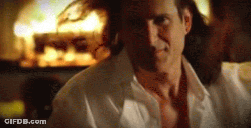 A Man In A White Shirt Is Standing In Front Of A Fire GIF