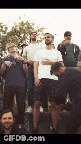 A Man In A White Shirt Is Standing In Front Of A Group Of People GIF