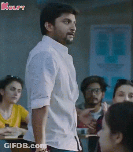 A Man In A White Shirt Is Standing In Front Of A Group Of People In A Classroom With The Word Kulfy On The Bottom GIF