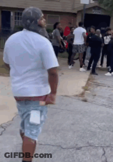 A Man In A White Shirt Is Standing In Front Of A Group Of People On The Sidewalk . GIF
